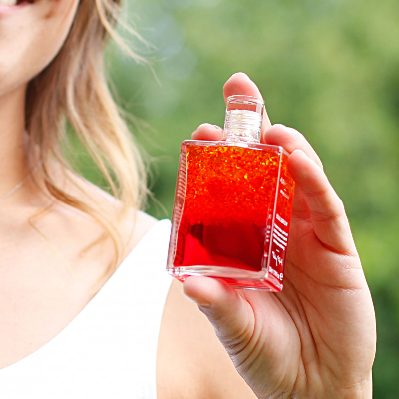 Eine lächelnde Frau hält die geschüttelte Aura-Soma-Flasche B5 in der Hand.